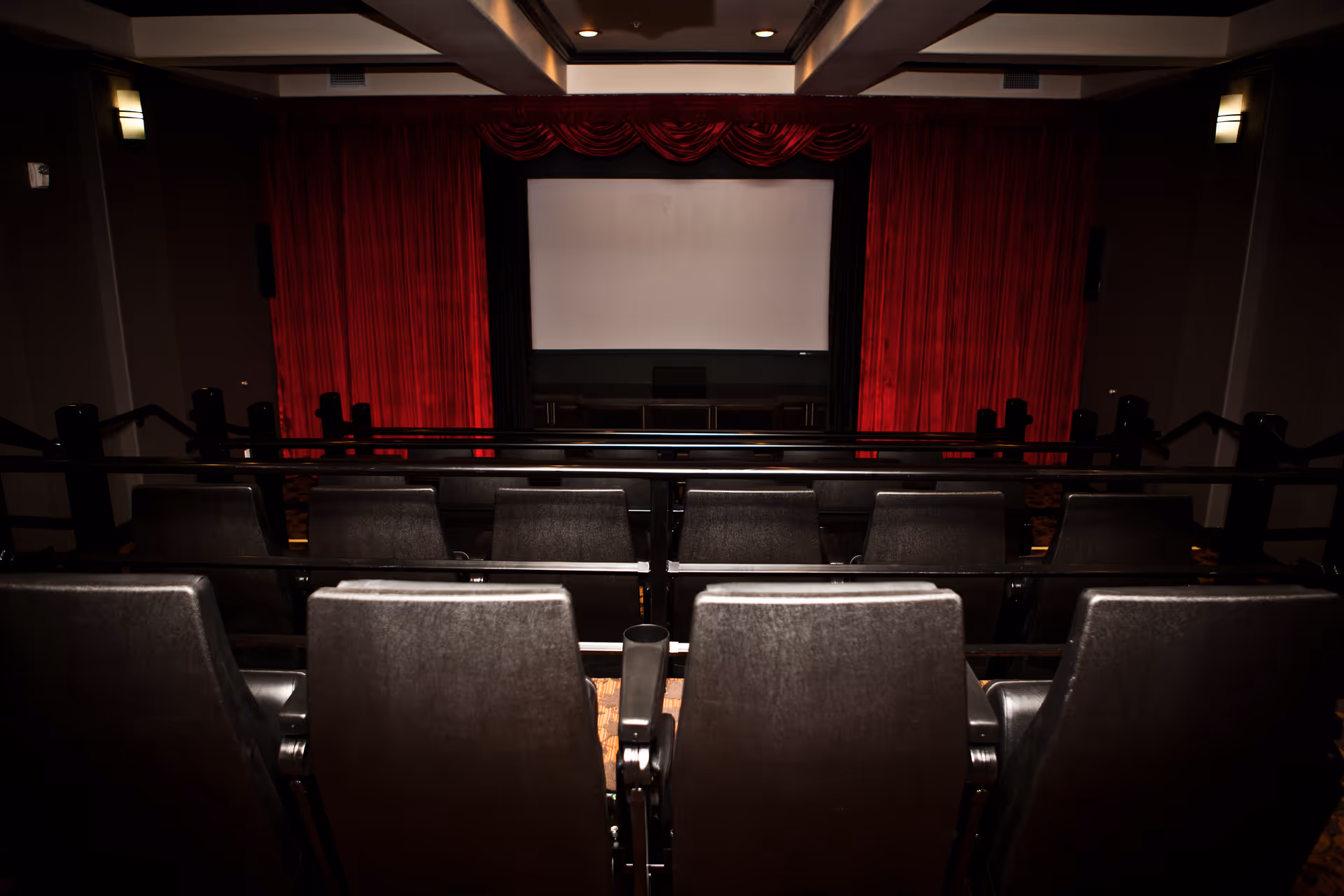 Small private theater with rows of black seats facing a white screen framed by red stage curtains.