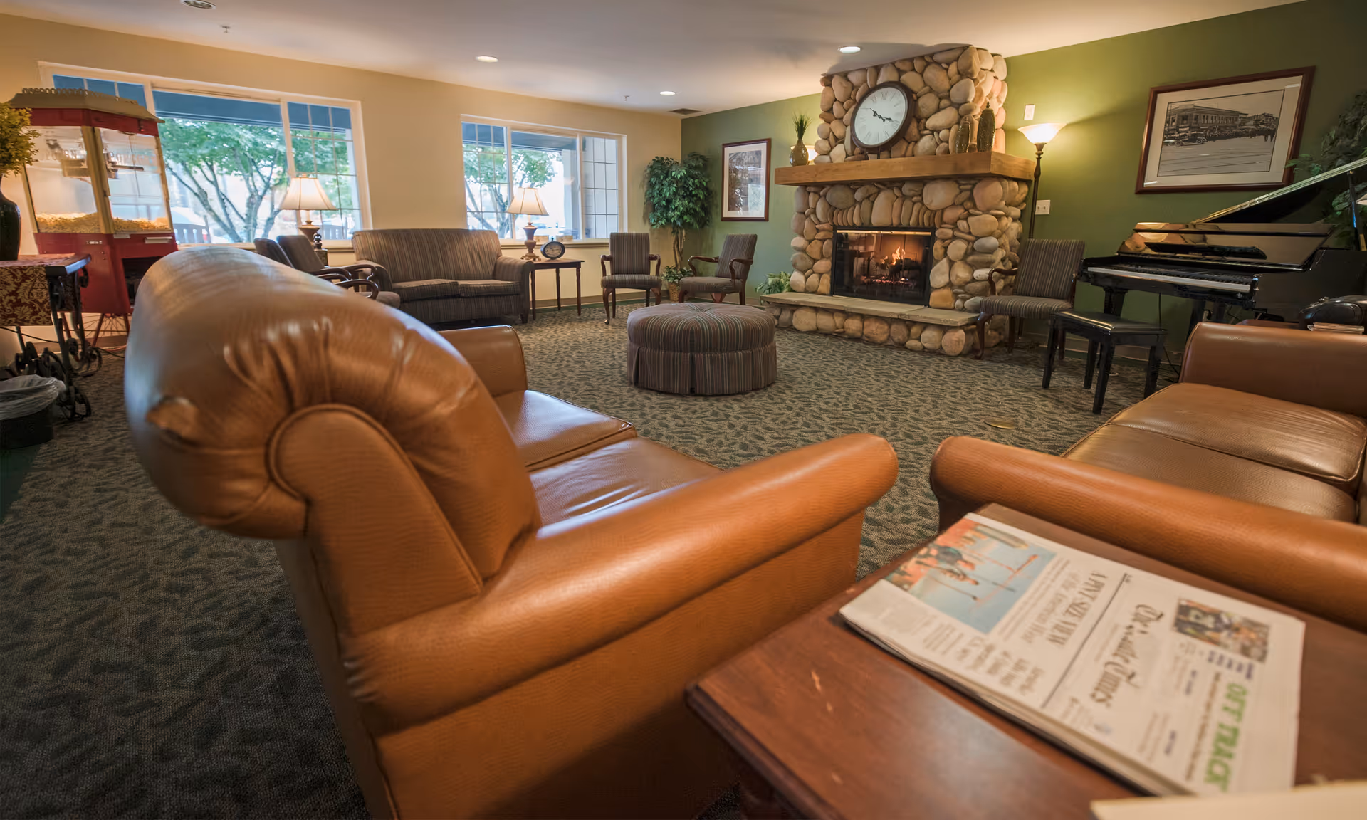 Cozy common living room with leather chairs and sofas arranged around a stone fireplace and piano.