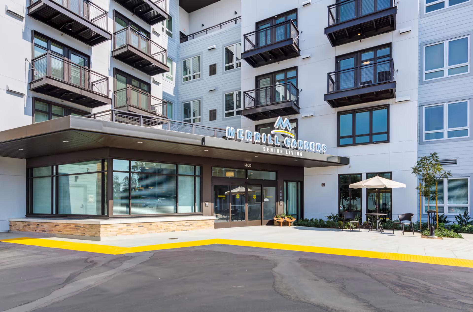 Entrance and facade of a multi-story Merrill Gardens senior living building with balconies and outdoor seating.