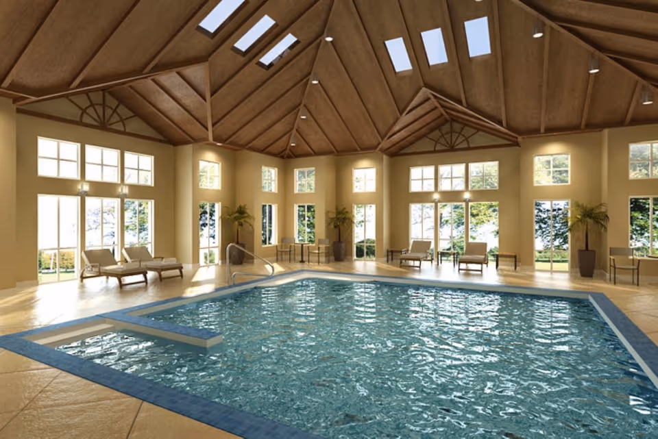 Indoor swimming pool room with lounge chairs, large windows, and a vaulted wooden-beam ceiling.