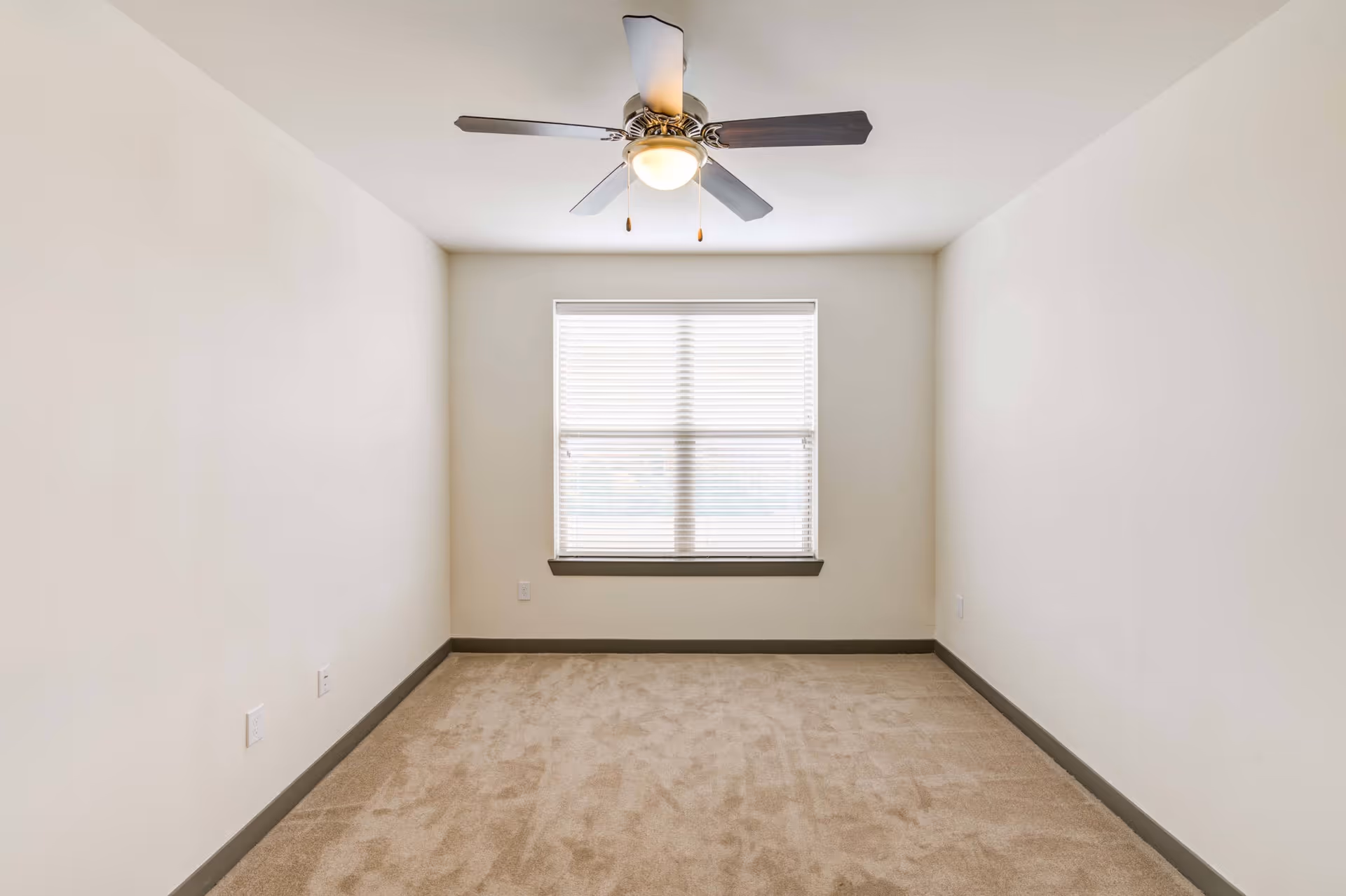 Empty bedroom with beige carpet, a ceiling fan, and a window with blinds.