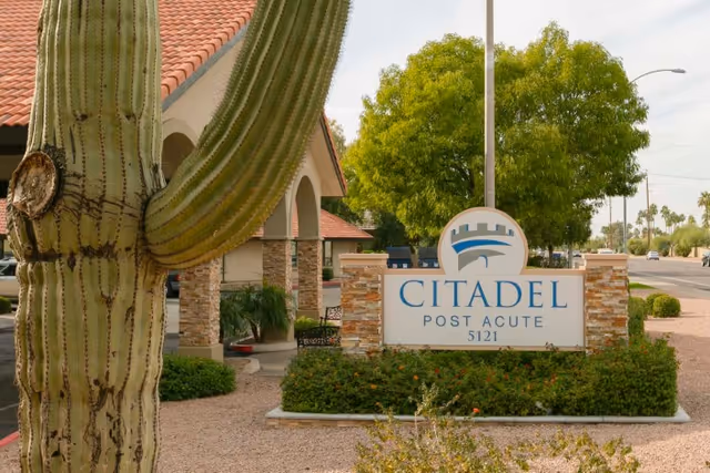 Exterior view of Citadel Post Acute facility with a large cactus in the foreground, a stone and stucco building with a red tile roof, and a sign displaying the facility name and address 5121 surrounded by greenery and trees.