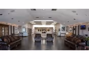 Spacious communal lounge with leather sofas, armchairs, coffee tables, and a reception area under recessed ceiling lights.