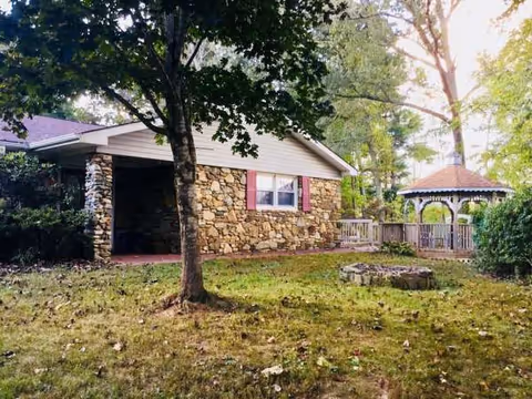 Stone-faced senior facility exterior with a front porch, trees, and a gazebo in the yard