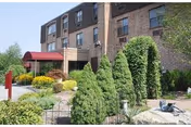 Brick senior care facility exterior with red awning entrance and manicured landscaping.