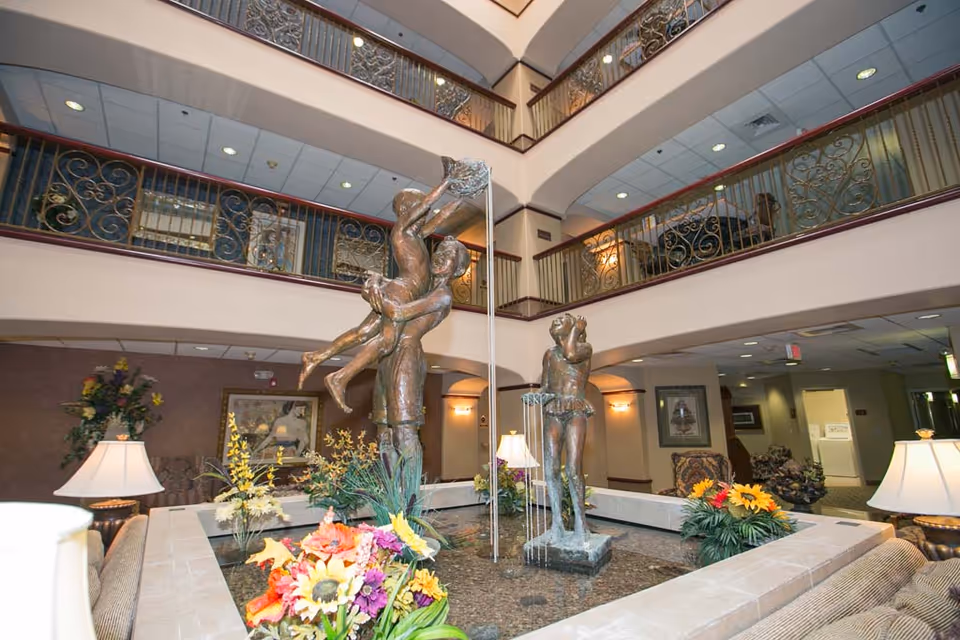Atrium lobby with a central fountain featuring bronze statues, surrounding seating and floral arrangements beneath mezzanine balconies.