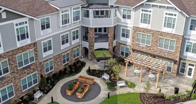 Landscaped central courtyard with raised wooden planters, benches, a pergola and seating surrounded by a multi-story senior living building.