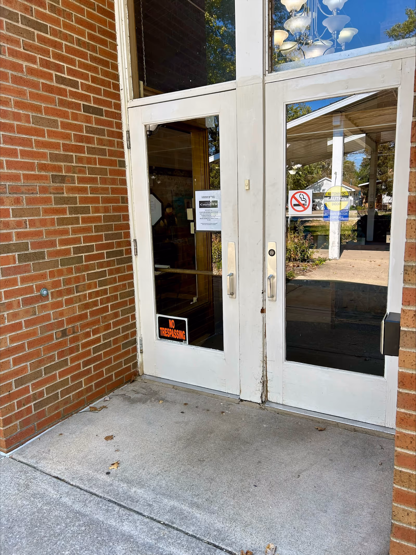 Double glass entrance doors set in a brick exterior with a 'No Trespassing' sign and notices on the glass.