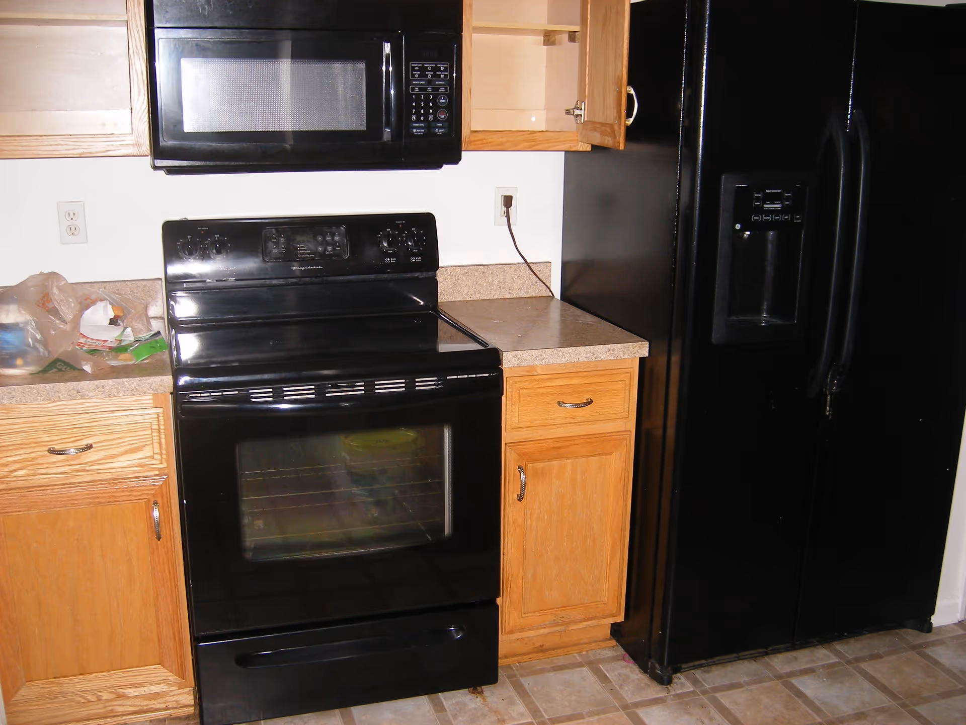 Kitchen showing a black stove and microwave between oak cabinets and a black side-by-side refrigerator.