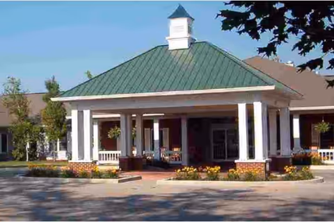 Front view of Hawthorne Inn, a senior living facility, with white columns, green roof, and entrance.