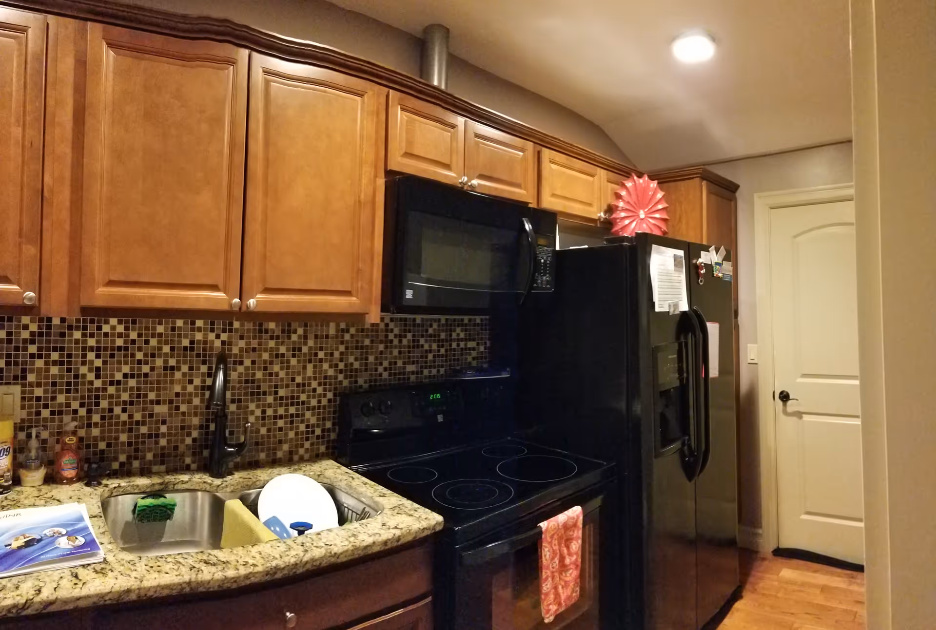 Kitchen with wooden cabinets, mosaic tile backsplash, granite countertop with sink, and black stove, microwave, and refrigerator.