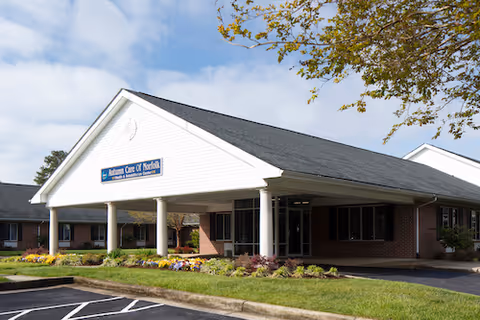 Front exterior of the Autumn Care of Norfolk building with a covered entrance, columns, and landscaped flowerbeds.