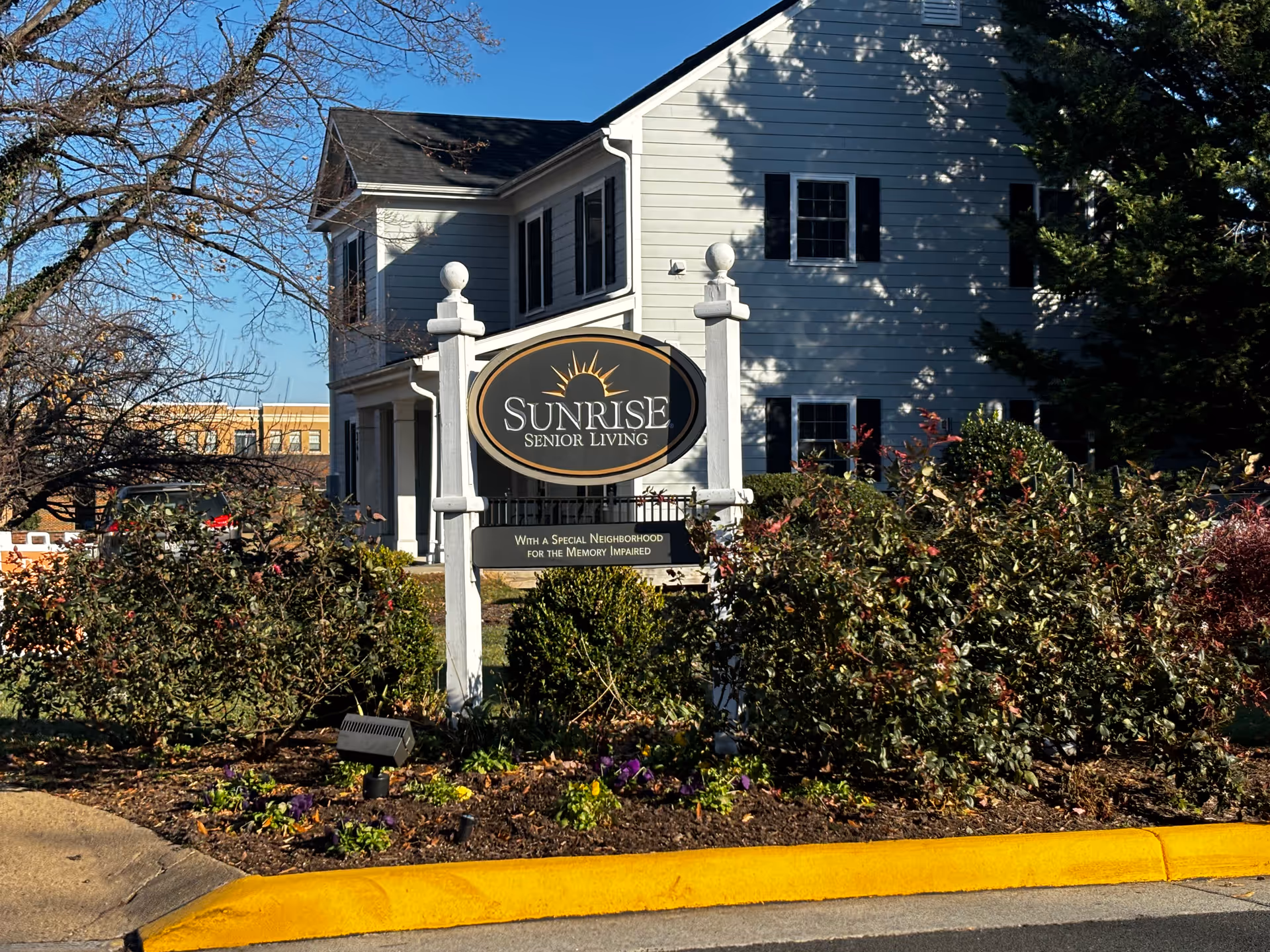 Sign reading 'Sunrise Senior Living' in a landscaped front yard of a two-story white building.