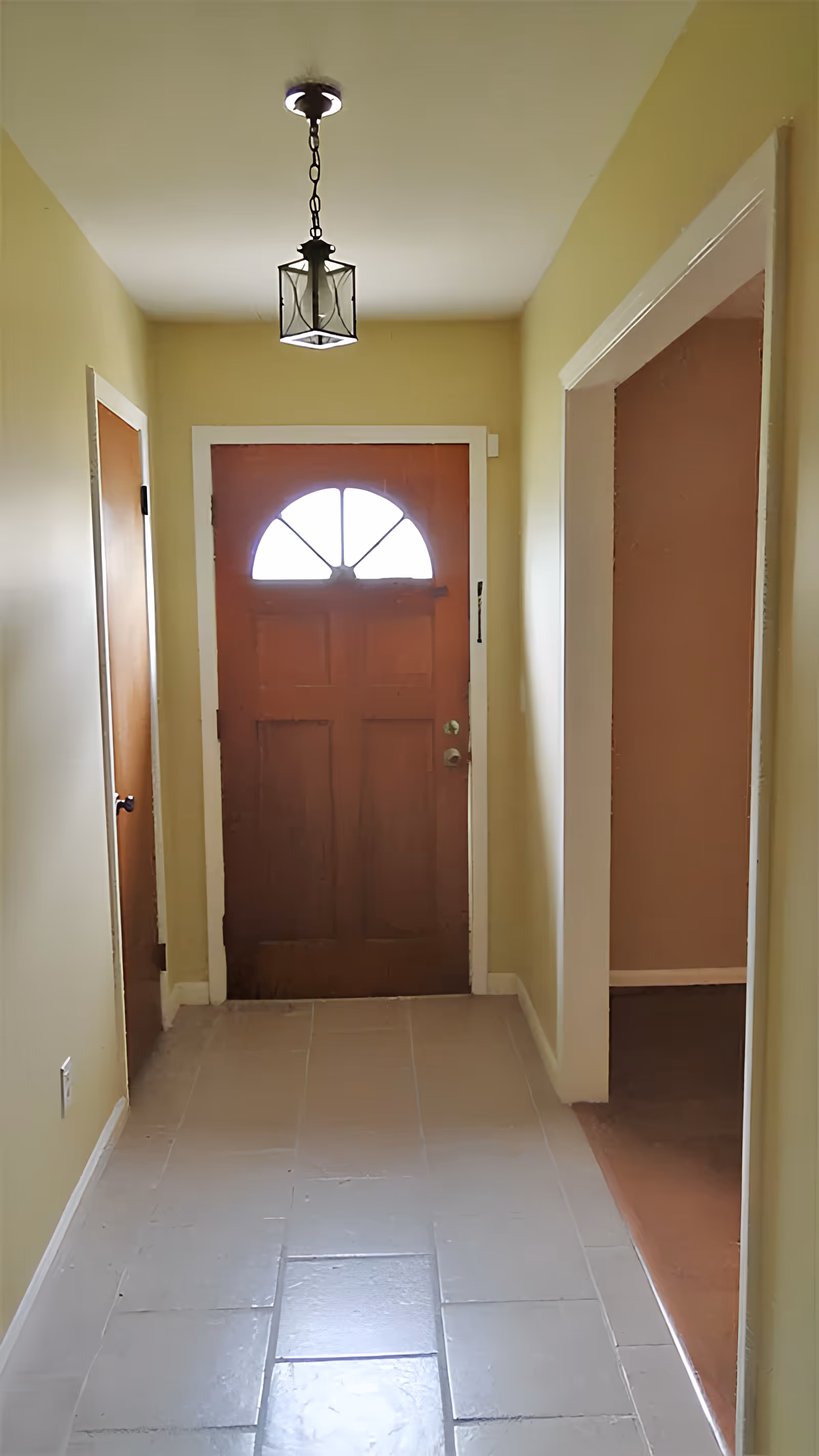 Narrow entry hallway with a wooden front door featuring a semicircular window, tiled floor, pendant light, and adjacent doorways.