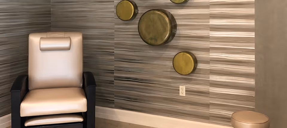 Modern padded armchair and small round stool against a striped wall with circular metallic wall art.