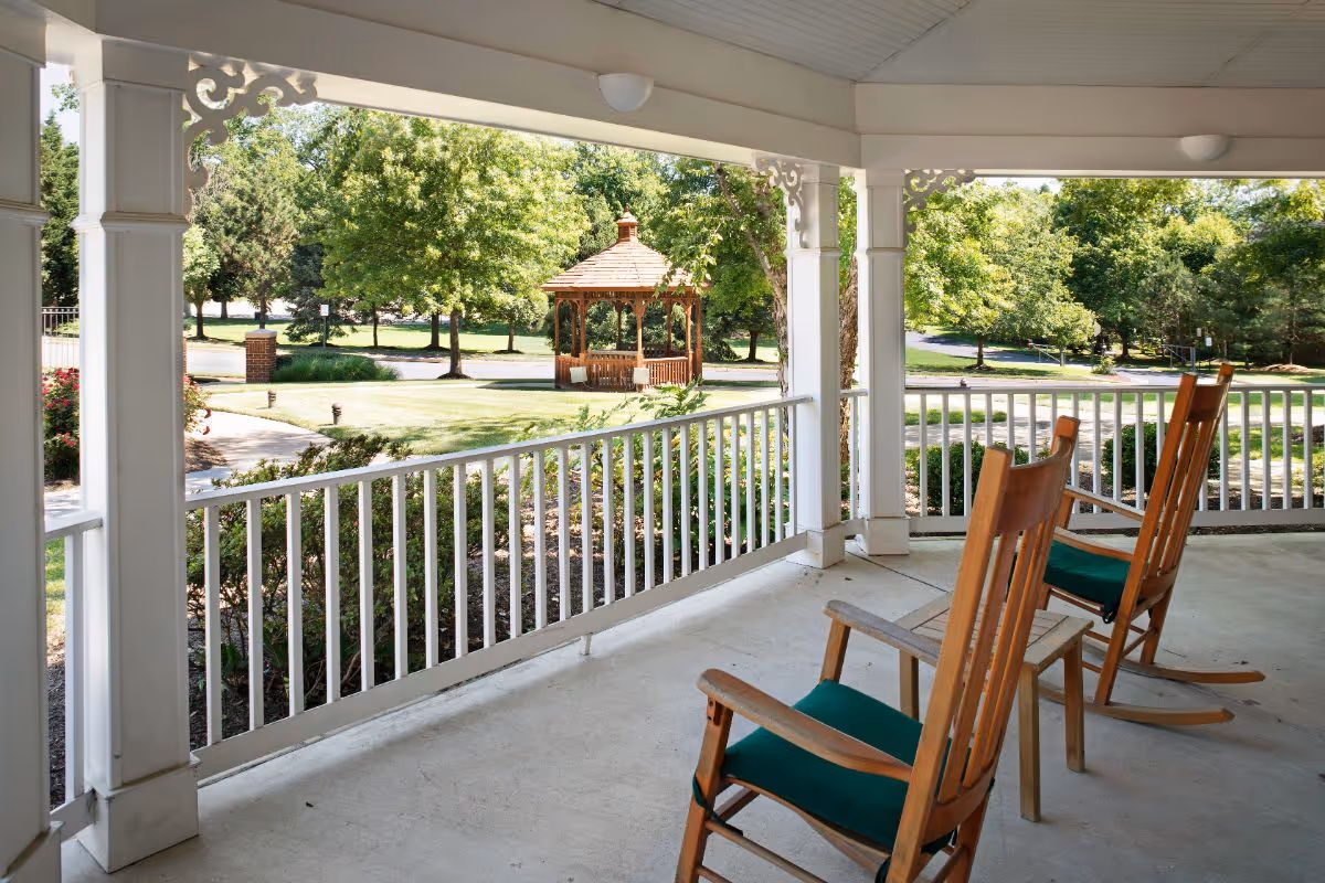 Covered porch with wooden rocking chairs overlooking a lawn and a gazebo.