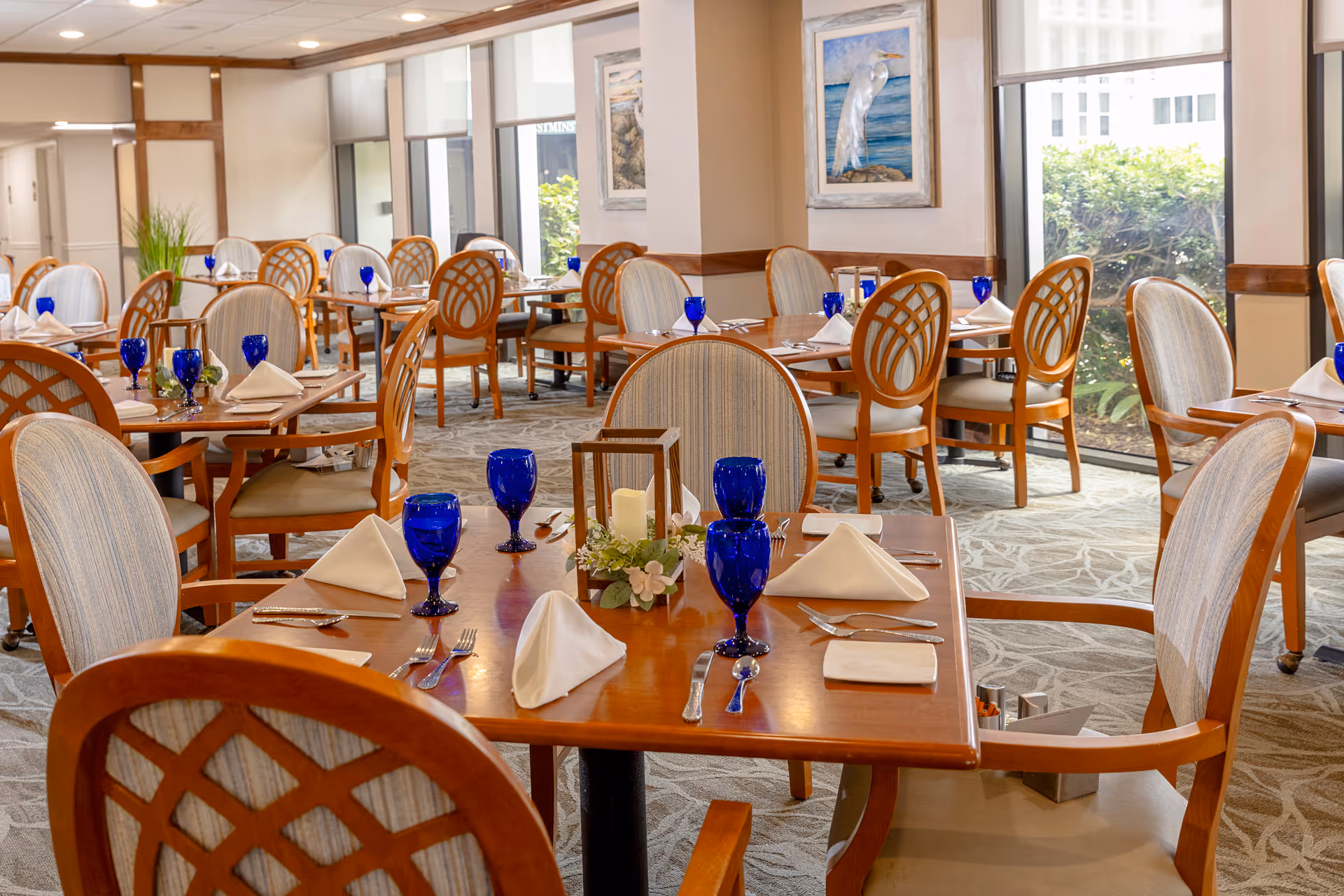 Bright dining room with wooden tables and chairs set with blue goblets and white napkins.