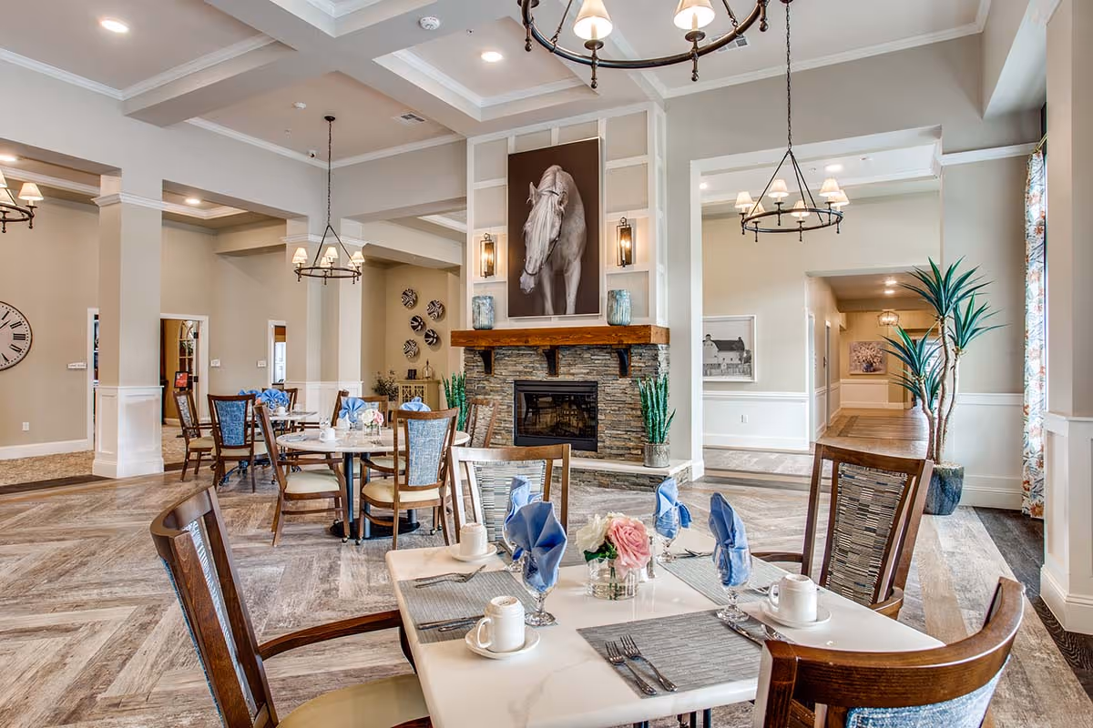Bright dining room with set tables, chandeliers, a stone fireplace and a large horse painting.