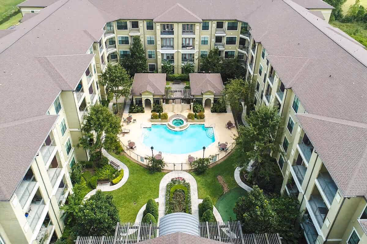 Aerial view of a U-shaped senior living building surrounding a landscaped courtyard with a swimming pool and hot tub.
