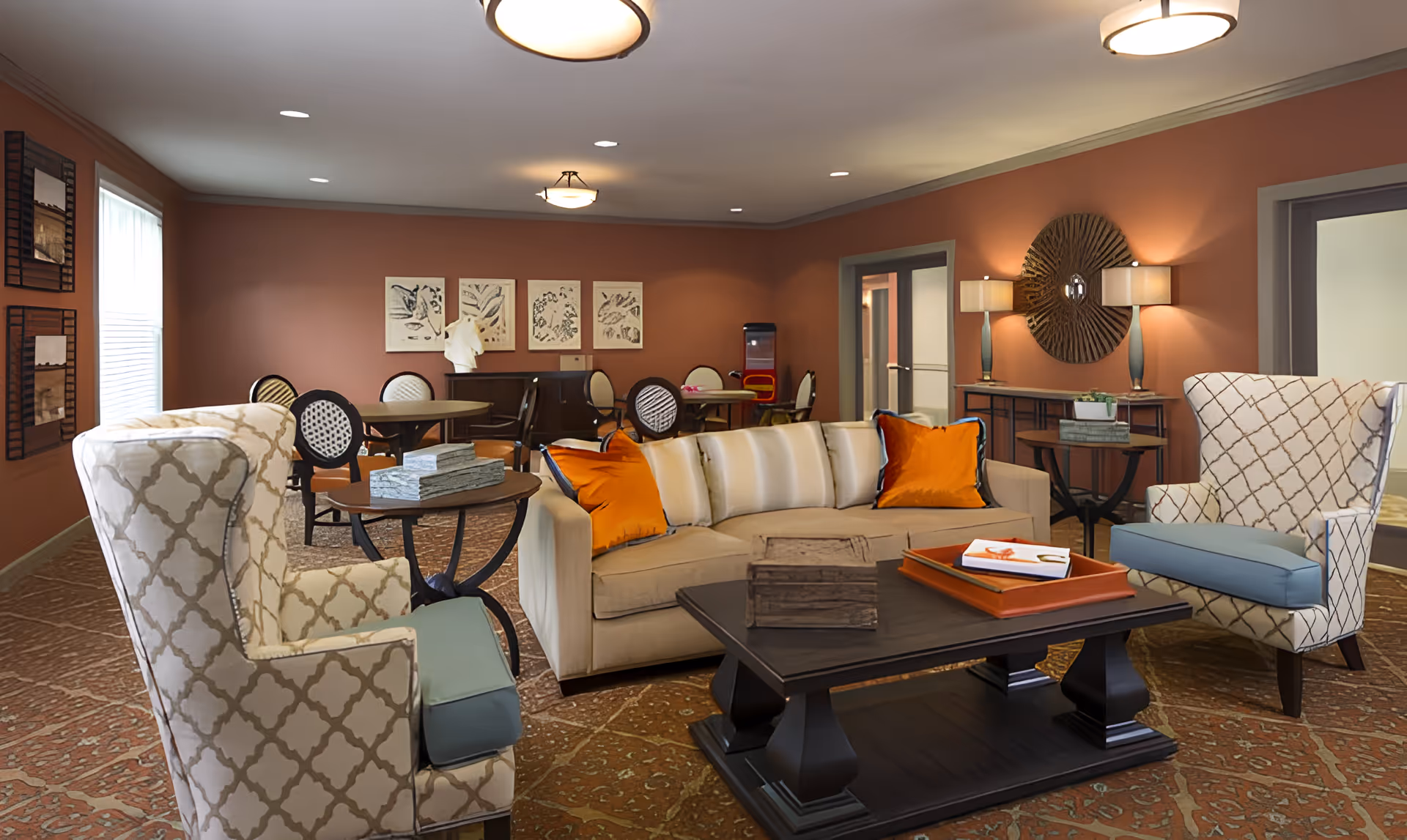 A warm communal lounge with a sofa, patterned armchairs, coffee table and dining tables in the background.