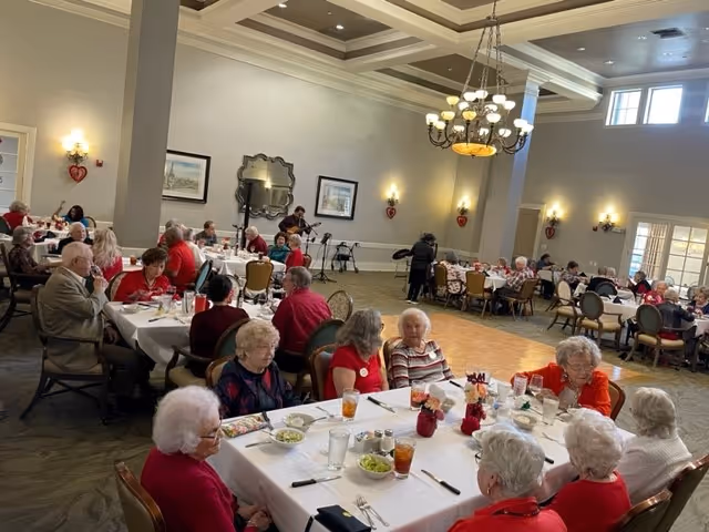 Elderly residents seated at decorated tables in a large dining room during a communal meal or event.