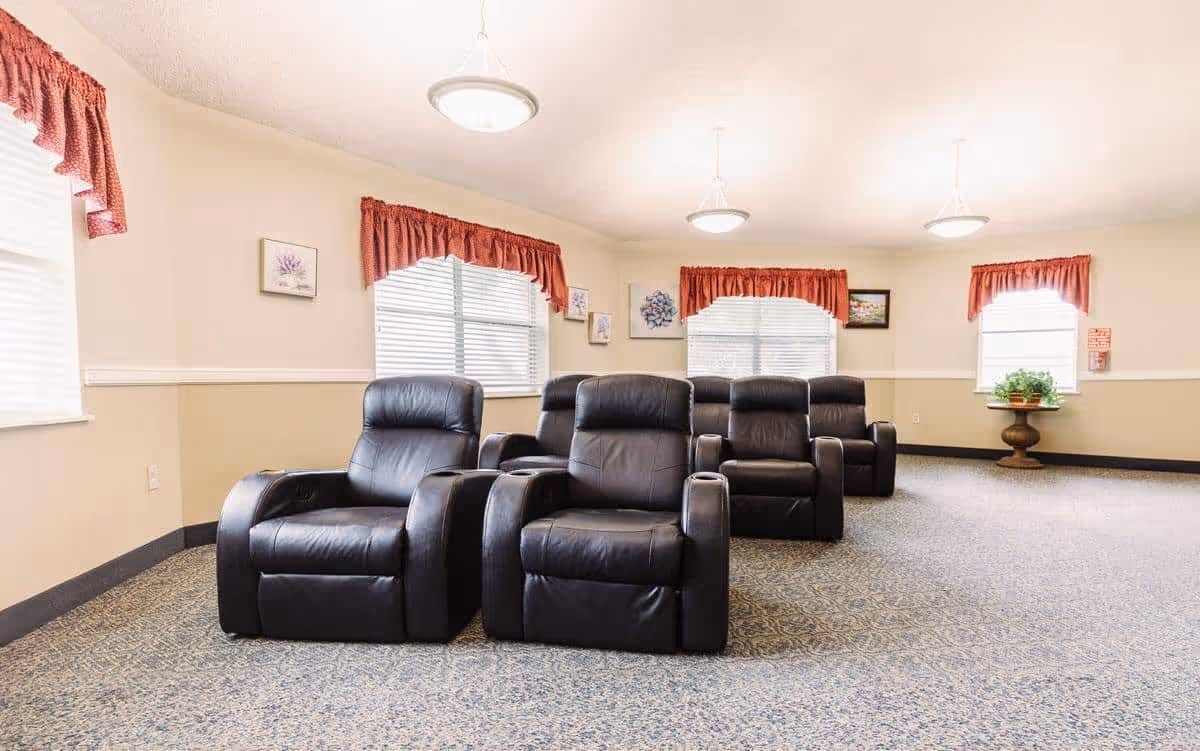 Row of black leather recliner chairs arranged in a bright common room with windows and red valances.