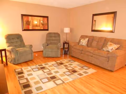 Cozy living room in a senior residential care facility with sofa, two armchairs, rug, and lighting.