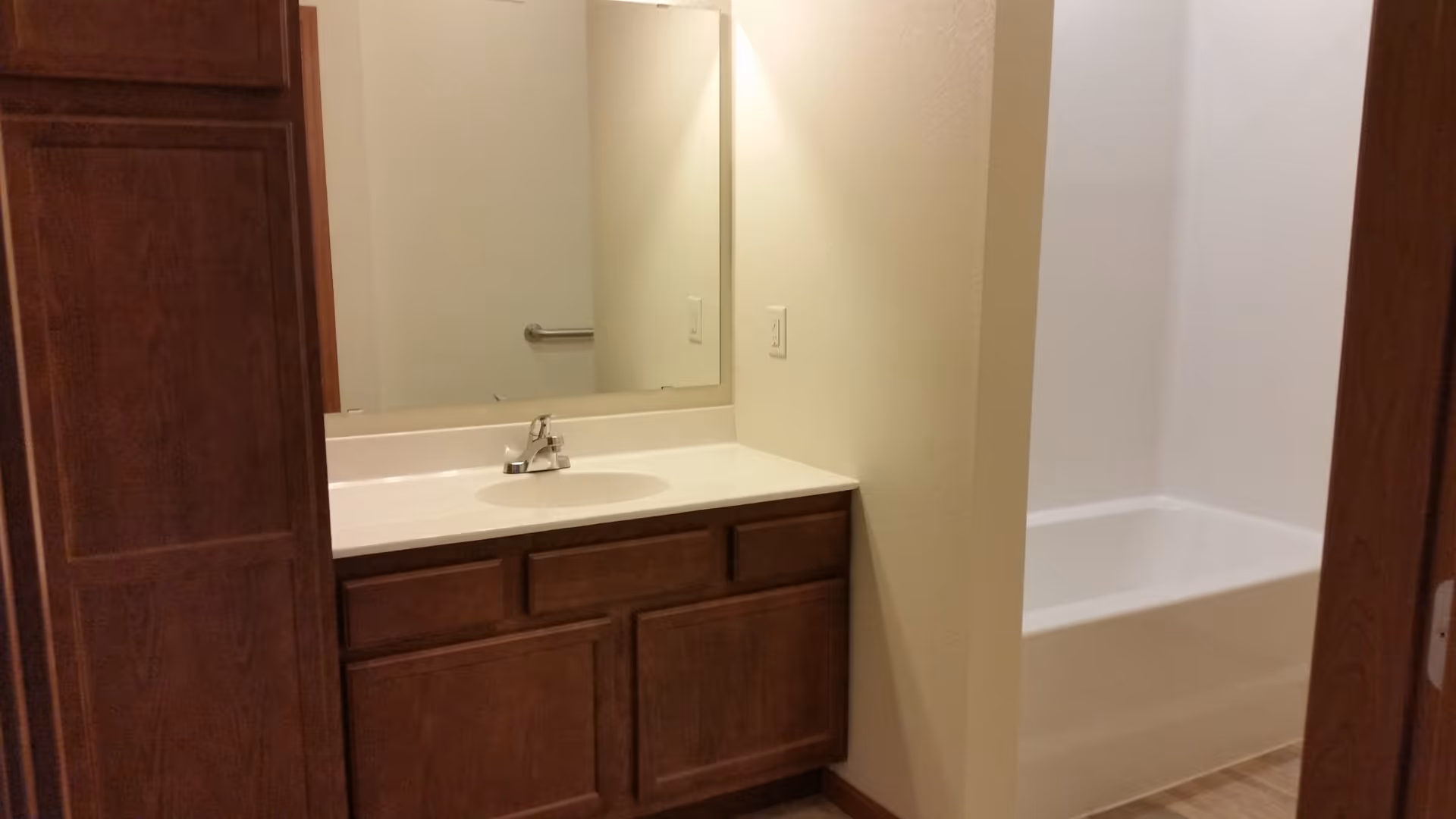 Bathroom showing a wooden vanity with a sink and mirror next to a white bathtub.