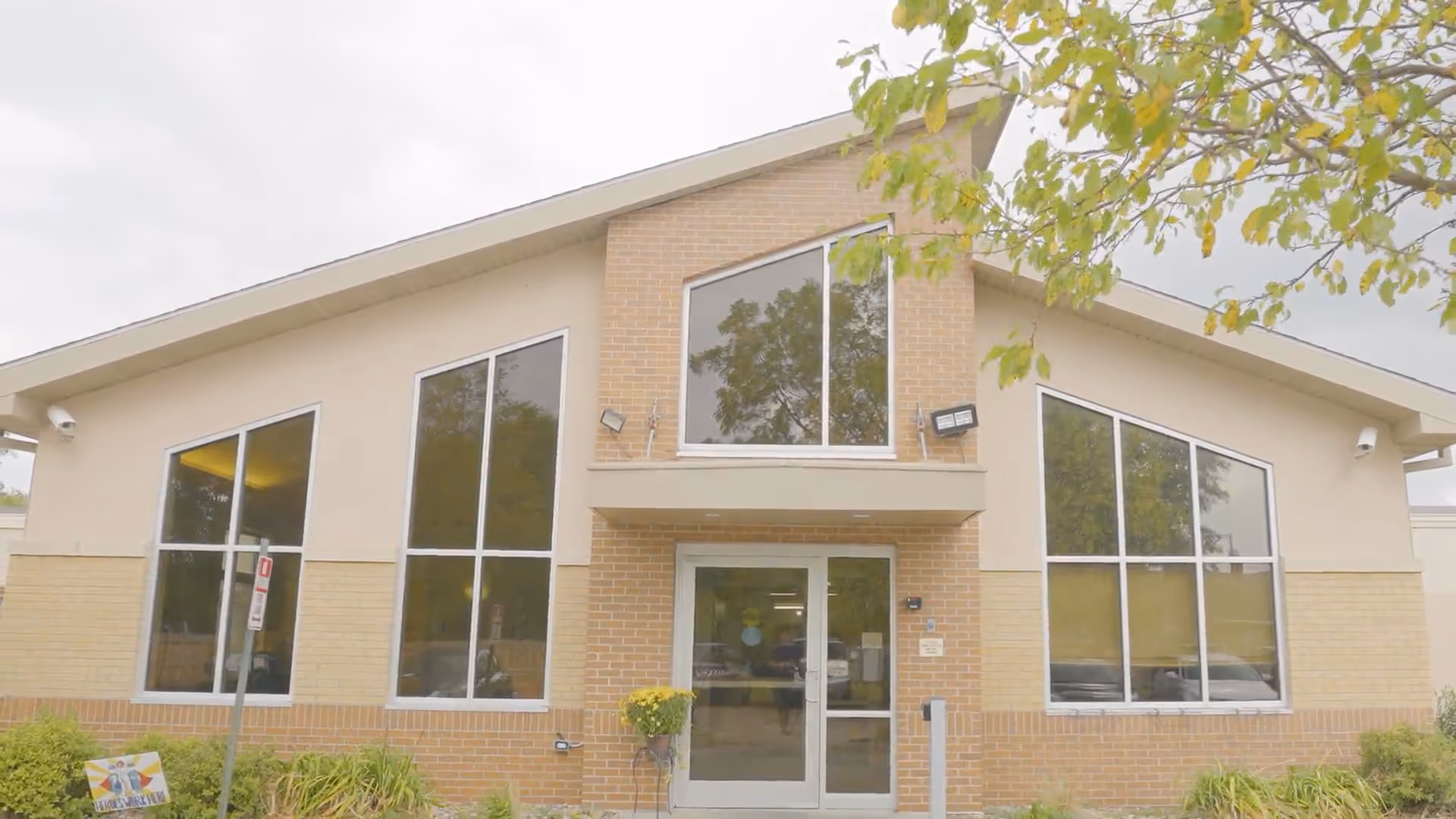 Front entrance of a single-story brick building with large windows, a glass door, and landscaping.