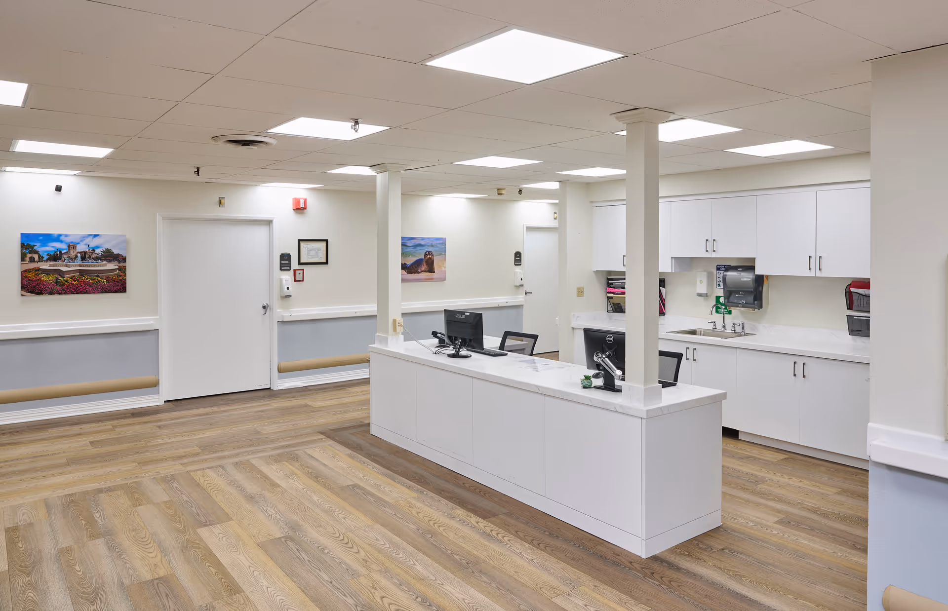 Bright reception/nurse station inside a nursing and rehabilitation facility with a long white counter, computers, and cabinetry.