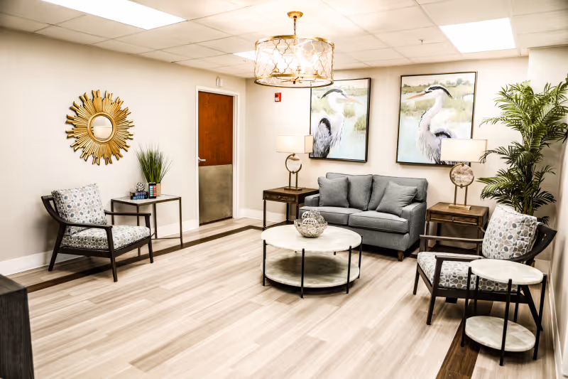 Bright lounge with a sofa, armchairs, round coffee tables, heron artwork, and decorative lighting.
