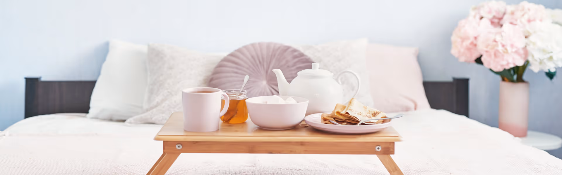 A breakfast tray with tea, honey, and pastries on a bed in a cozy room.