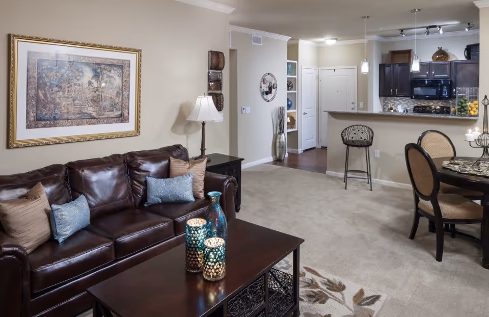 Open-concept living room with a brown leather sofa, coffee table with decorative vases, and an adjacent dining area and kitchen.