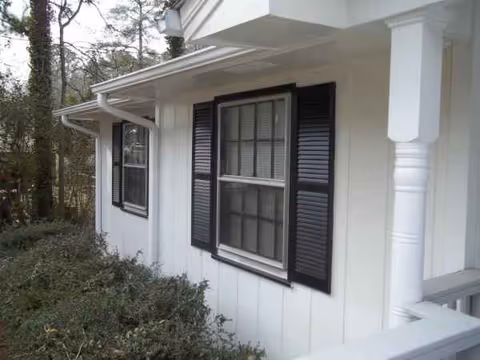 Exterior view of a white building with black window shutters and a porch railing.