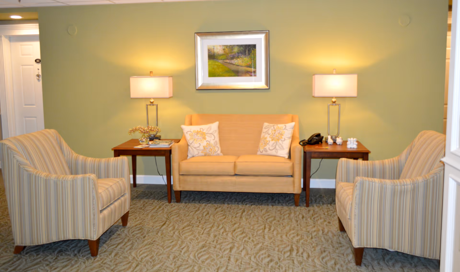 Small seating area with a loveseat flanked by two striped armchairs, side tables with lamps, and a framed painting on a green wall.