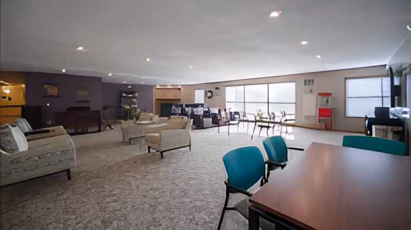 Spacious senior living common room with multiple seating areas, tables, a fireplace and large windows.
