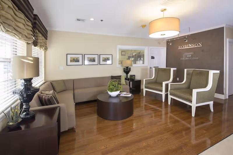 An inviting lounge area with a sofa, chairs, and light decor in Robinson Nursing and Rehabilitation Center.