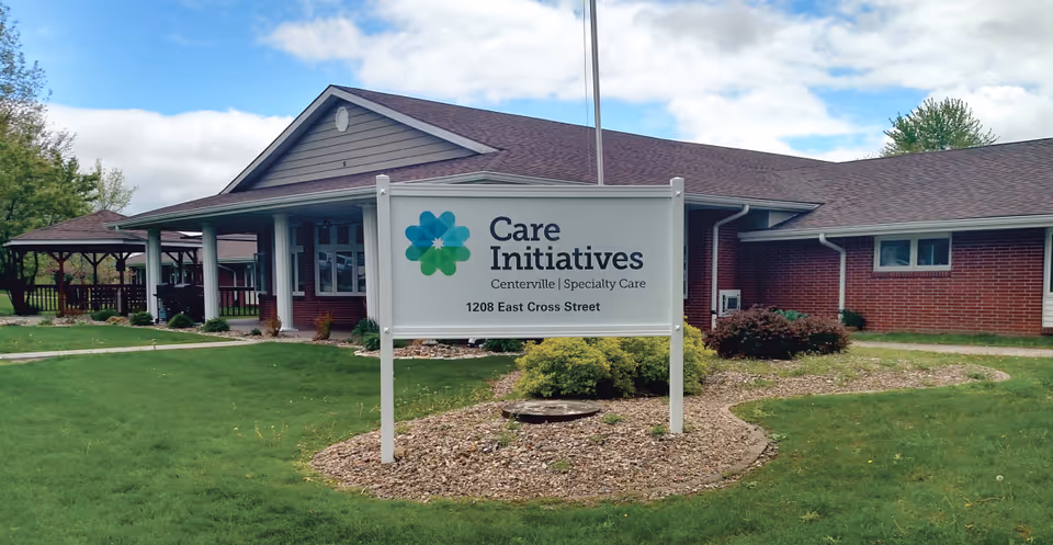 Exterior view of Care Initiatives Centerville Specialty Care building with a sign in front displaying the facility name and address 1208 East Cross Street. The building has a brick facade, a covered entrance, and a well-maintained lawn with landscaping.