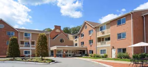 Brick senior living building with an entrance canopy, driveway, and manicured landscaping.