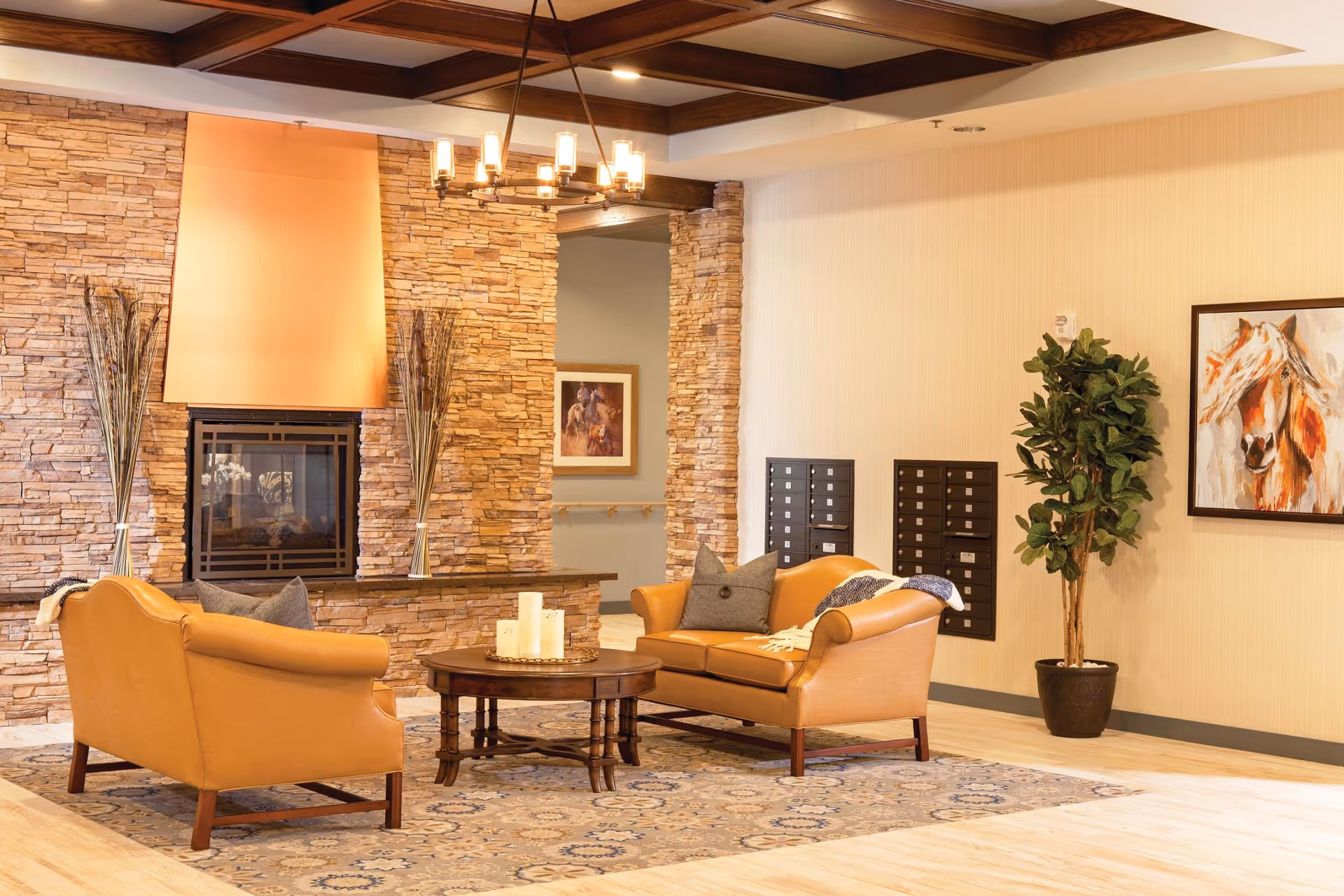 Cozy common area with two tan leather sofas around a round coffee table in front of a stone fireplace and decorative artwork and plants.