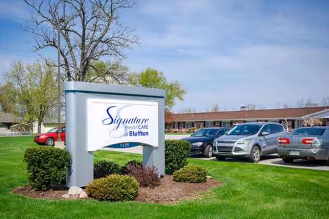 Exterior view of Signature HealthCARE Bluffton with sign, manicured lawn, and parked cars.