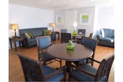 Common room with a round table and chairs, sofas, side tables with lamps, and framed artwork on the walls.