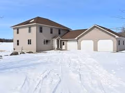 Two-story beige home with a three-car garage surrounded by snow on a clear day.