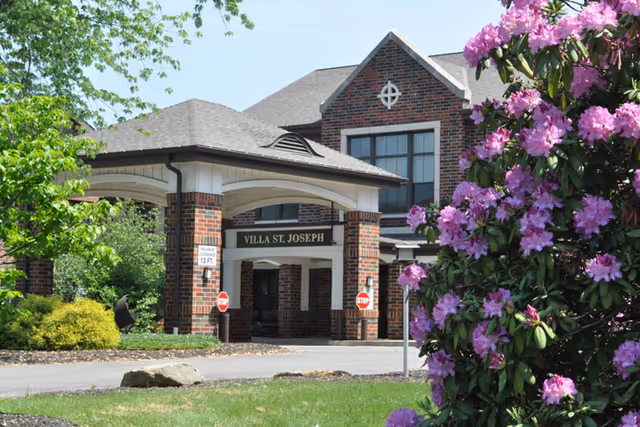 Entrance of Villa St. Joseph building with a covered porte-cochere and a large pink flowering bush in the foreground.
