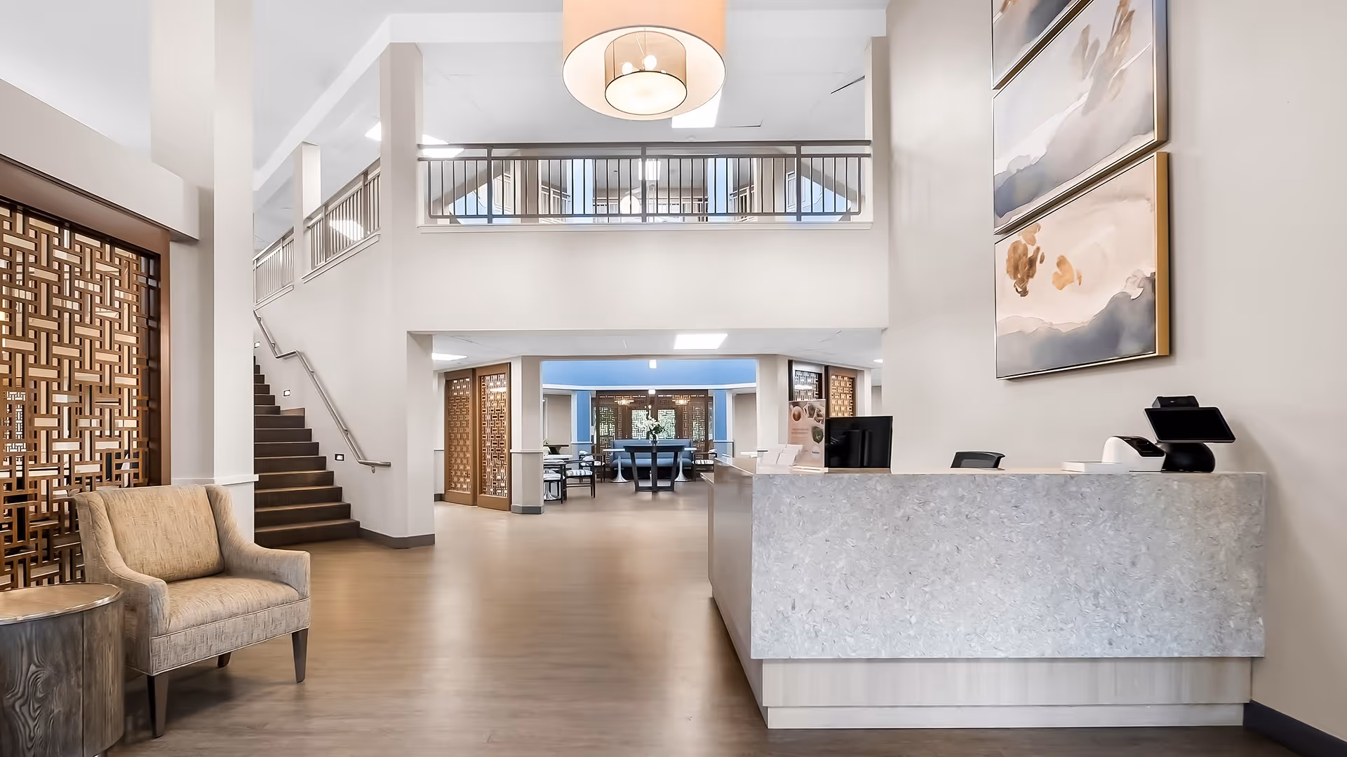 Spacious senior living lobby with a reception desk, seating area, staircase, and an open second-floor balcony.