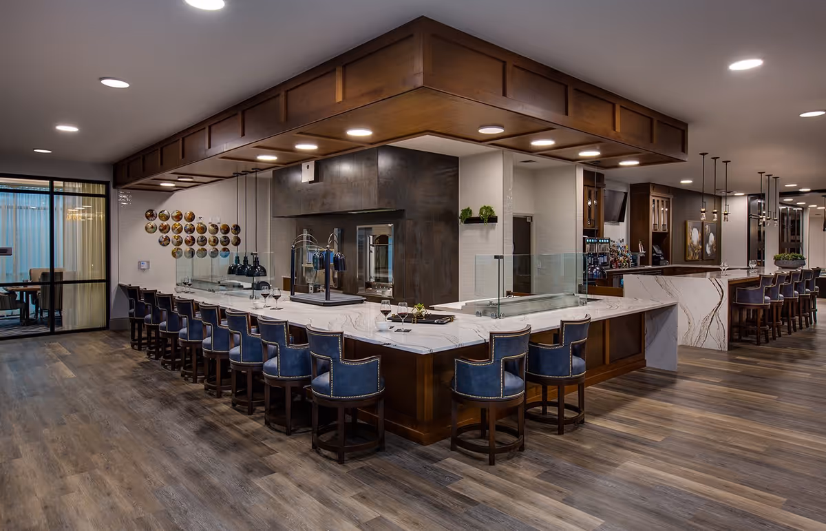 Spacious modern dining and bar area with a long marble counter lined with blue upholstered bar stools and wood flooring.