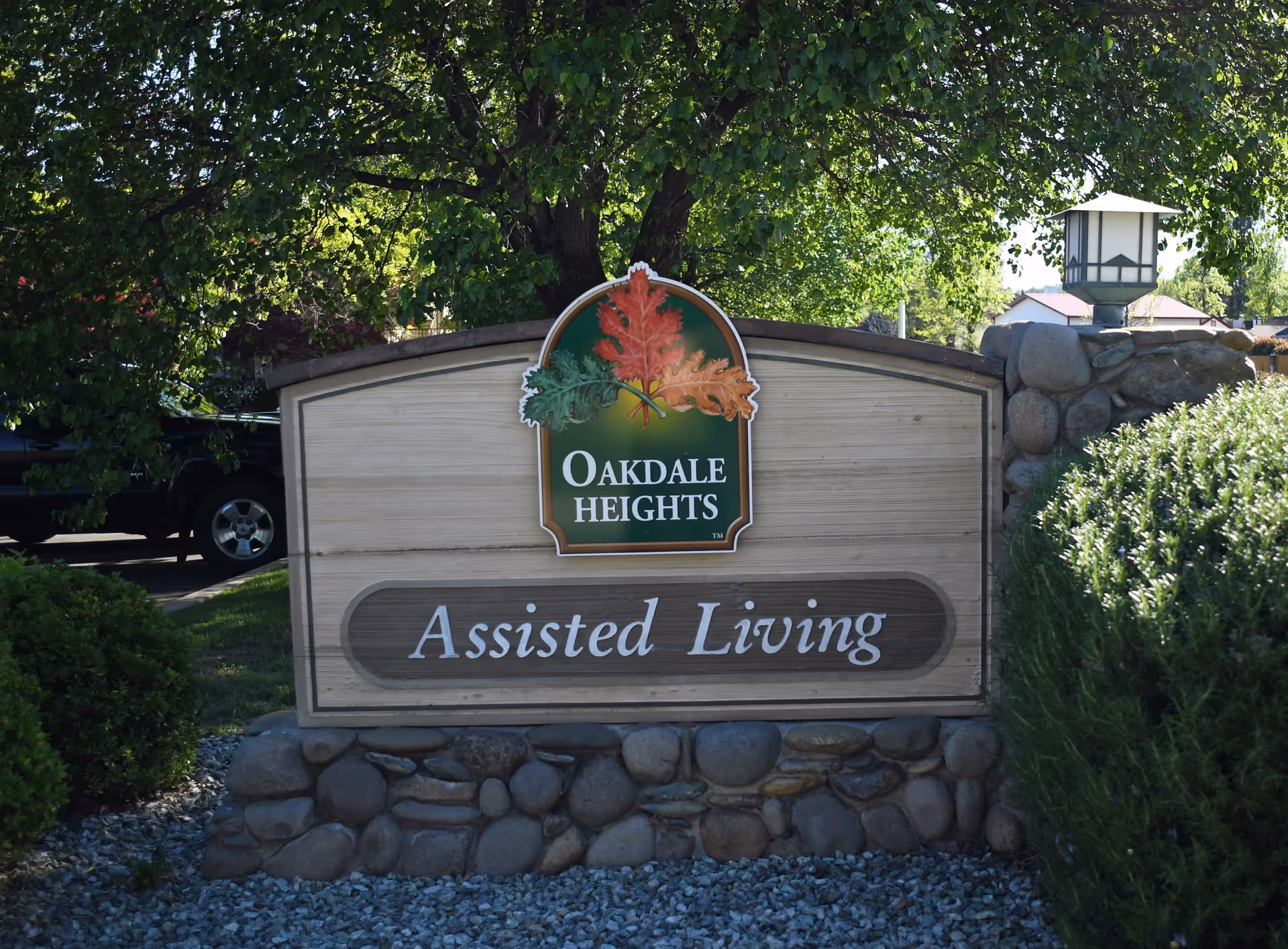 Outdoor sign for Oakdale Heights Assisted Living, featuring a wooden board with a stone base, surrounded by greenery and a tree in the background.
