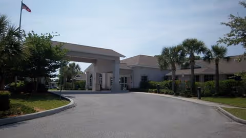 Front exterior of Magnolia Gardens ALF with driveway, entrance canopy, and palm trees.