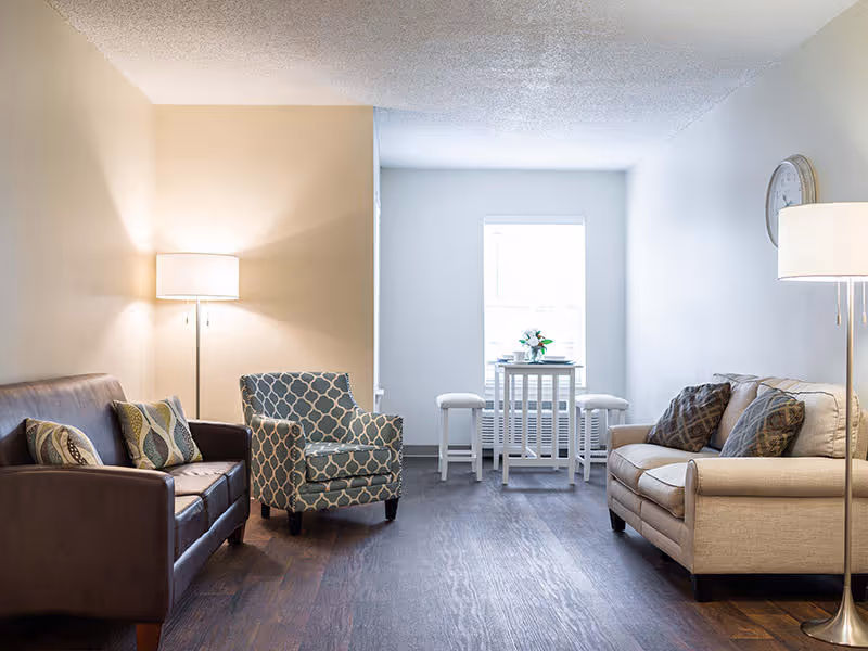 Bright furnished living room with two sofas, an accent chair, floor lamps, and a small table by a window.
