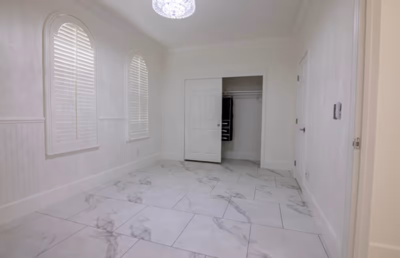 Empty bright bedroom with marble-pattern tile floor, arched shuttered windows, a chandelier, and an open closet.